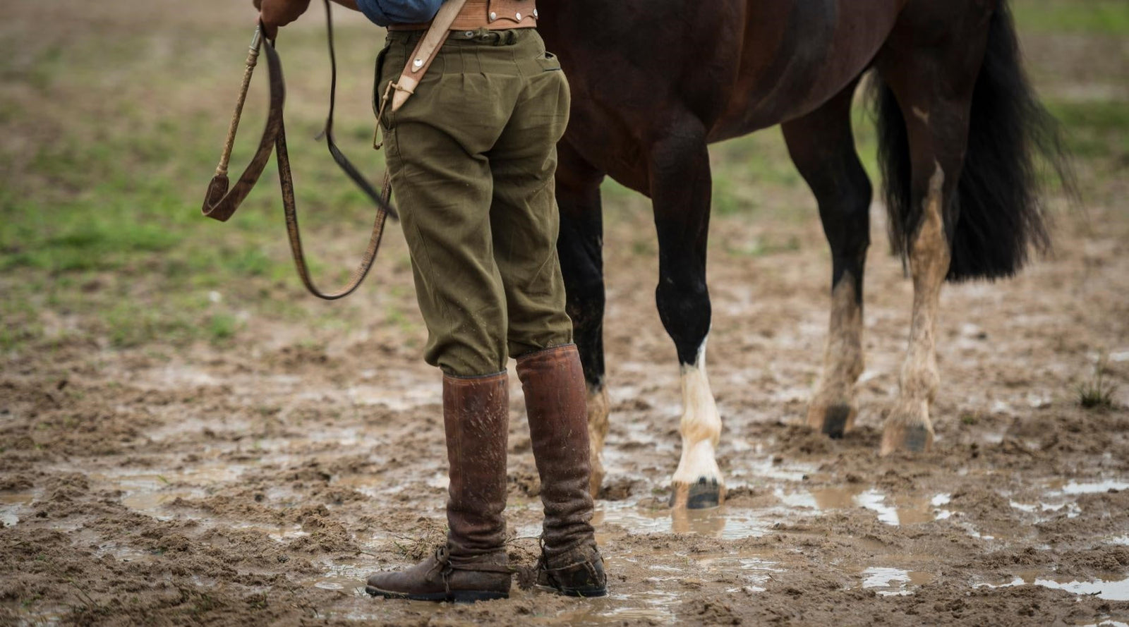 Rider and horse standing in muddy paddock. Wet and muddy winter conditions can cause Mud Fever, Greasy Heel, Scratches & Rain Scald - officially known as Pastern Dermatitis.